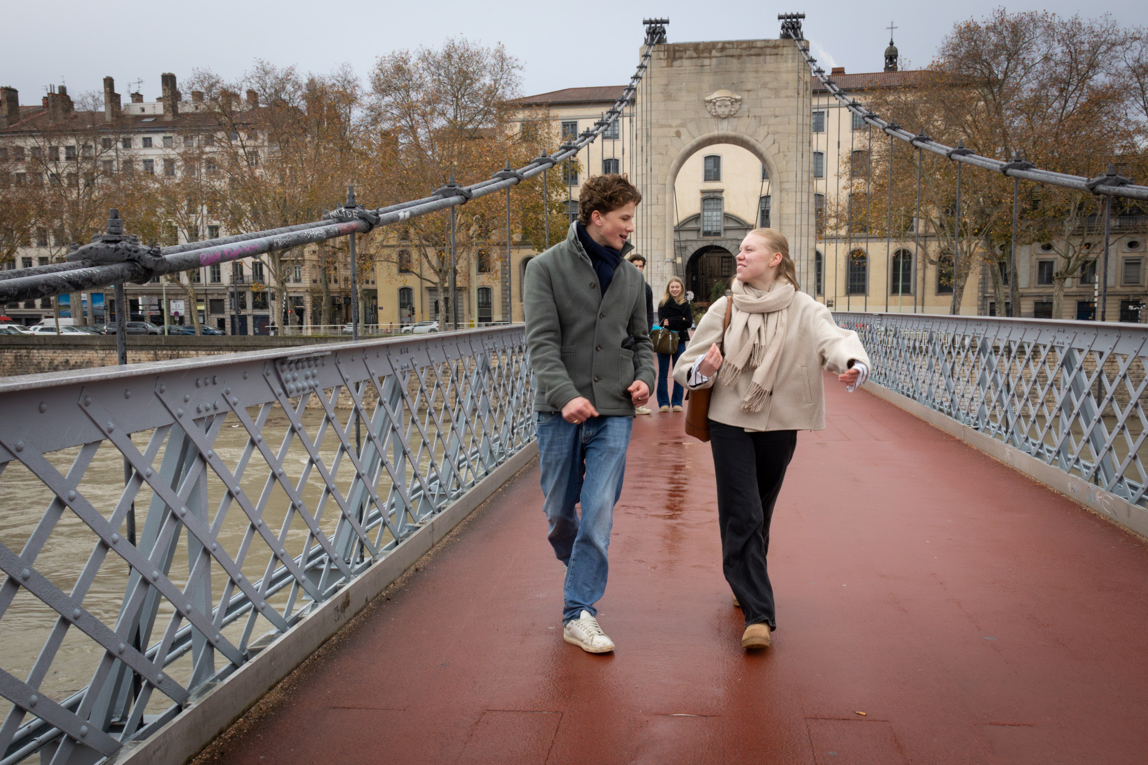 To ungdommer går og prater sammen over en rød gangbro i en by.
