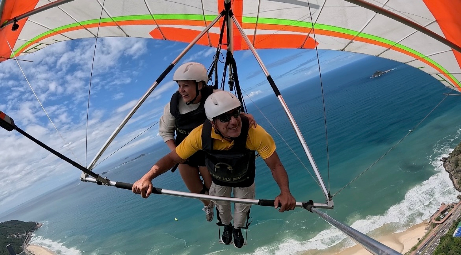 Kvinne iført hvit genser og hjelm er på paragliding sammen med instruktør med hvit hjelm og gul T-skjorte.