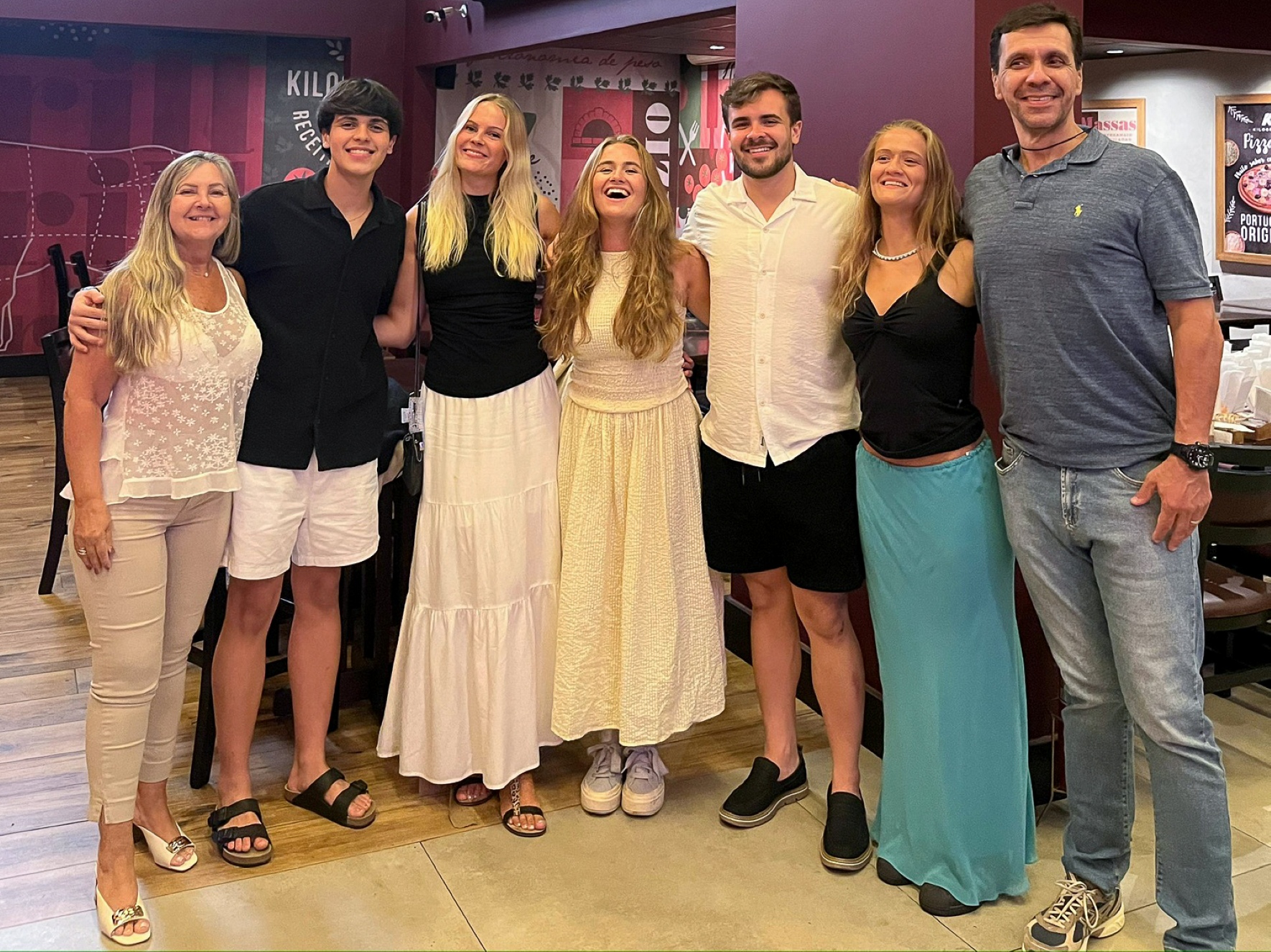 Gruppebilde. Utvekslingsstudent Frida står som nummer tre fra høyre. Hun har langt blondt hår og er iført svart T-skjorte og hvit lang kjole. I bakgrunnen ser man et restaurantmiljø.