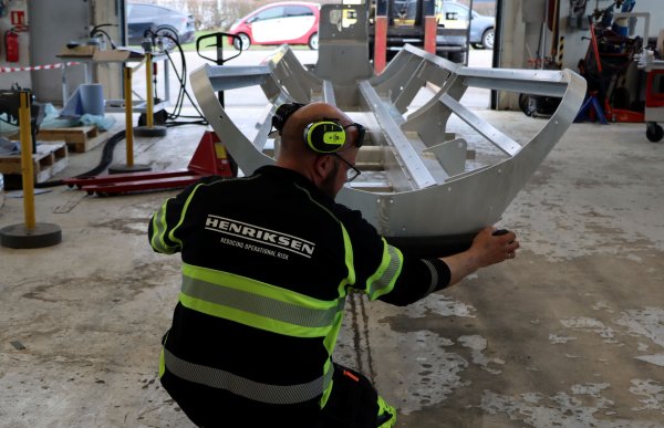 En mann sitter på huk foran en konstruksjon. Han er kledd i svart og signalgult. 