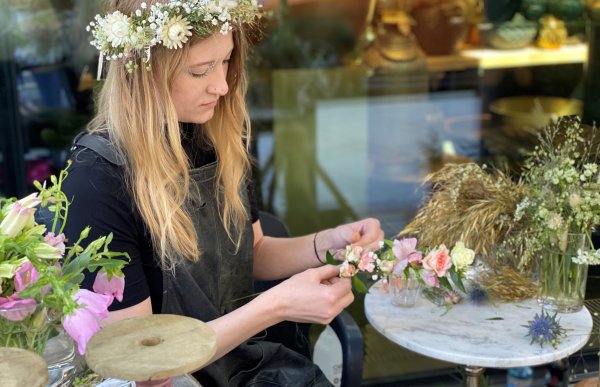Blomsterdekoratør Ingrid Marie Aarre med blomsterkrans i håret lager en blomsterkrans med rosa blomster