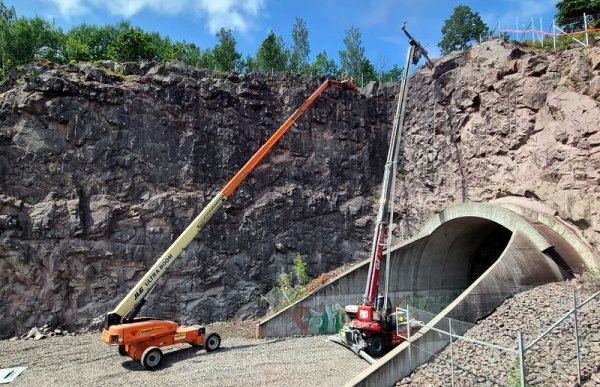 Bildet viser to store anleggsmaskiner som rensker fjellsiden ved inngangen til en tunell. 