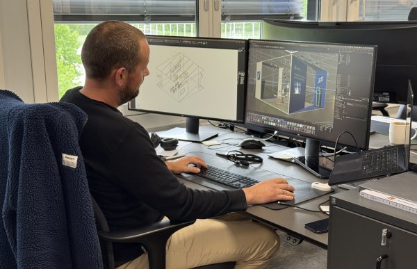 En mann i mørk genser sitter ved dataskjerm og jobber med tredimensjonale modeller. Han er på et kontor.