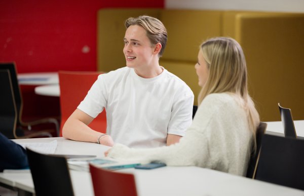 En blond gutt i hvit t-skjorte sitter ved et bord sammen med en blond jente med hvit genser