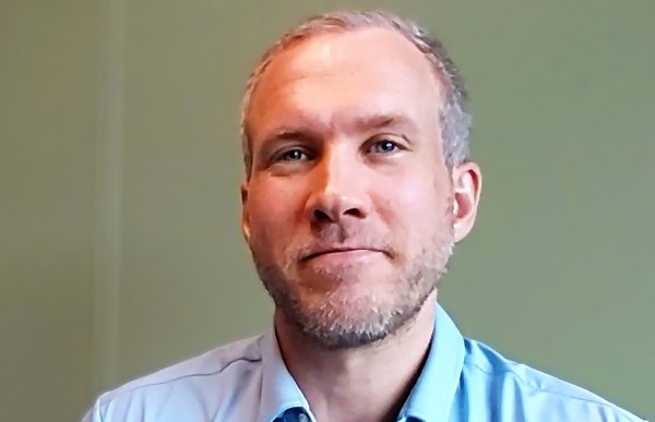 En mann i et lyseblå skjorte. Han smiler og ser rett i kameraet. 