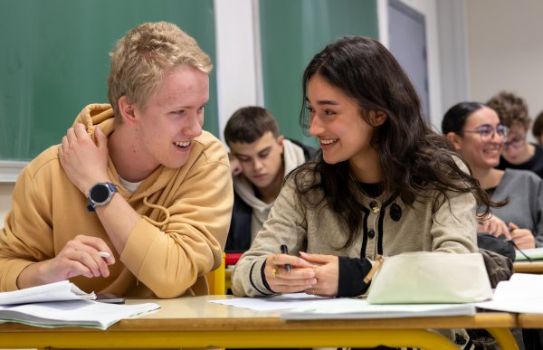 En ung mann og en ung kvinne ser på hverandre og prater. De er i et klasserom.