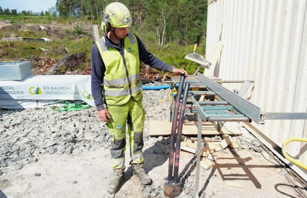 En brønnborer i refleksklær, hjelm og hørselvern håndterer boreutstyr på en byggeplass.