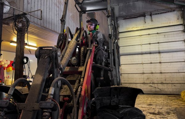 En mann med caps og briller sitter inne i en minilaster med en port i bakgrunnen. 