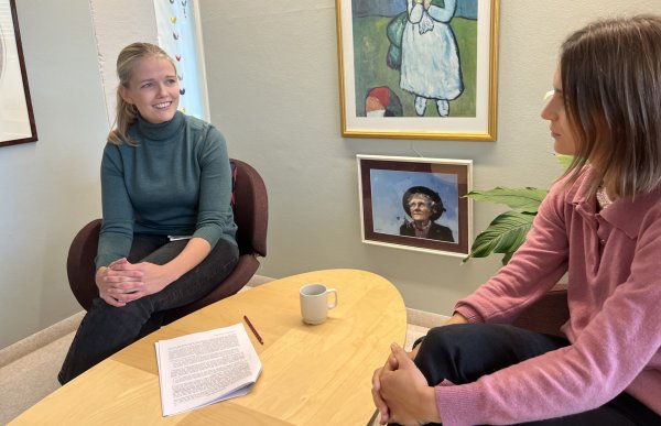 En kvinne i grå genser og en kvinne i rosa genser sitter ved et bord og har en samtale.