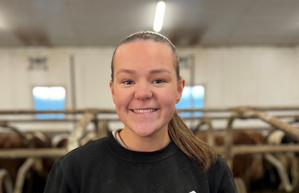 En person i svart collegegenser og hestehale. Hun er i en fjøs.