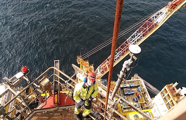 En mann i gul arbeidsdress og hjelm står på dekk på en borerigg ute i havet.