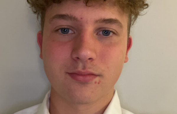 En mann i hvit trøye og blond hår står foran en hvit vegg