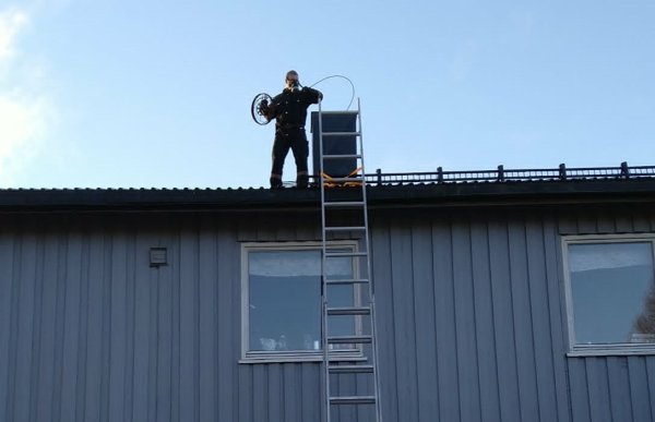 En person i mørke klær står ved en murpipe på taket av et hus.