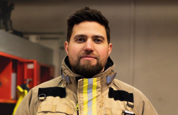 En mann med mørkt hår og skjegg. Han har på seg utrykningsdrakt. Han er inne.