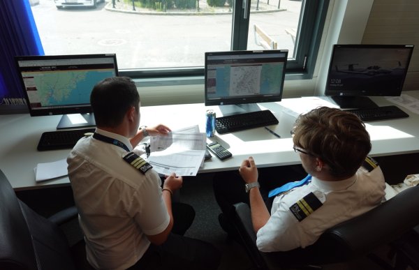 Mannlig flyinstruktør sammen med mannlig student foran pc. De sitter og ser på et kart over værforholdet i området.