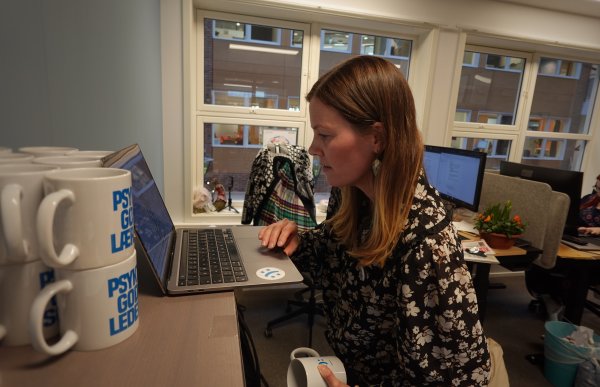 Kvinne står med en pc, leser av skjermen og ved siden av henne står et par kopper.