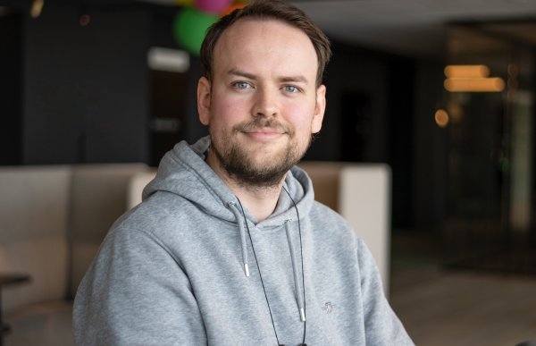 Smilende mann i grå hettegenser med ballonger bak seg.