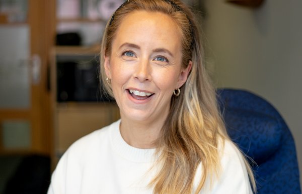 Profilbilde av en kvinne i hvit genser sitter på en blå kontorstol.