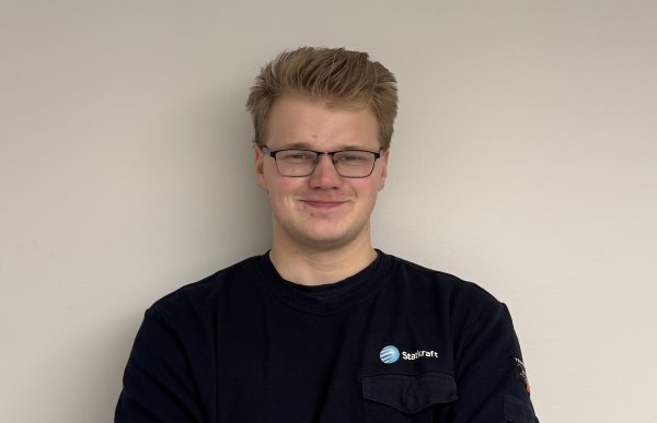 En mann med kort hår og briller og svart college genser. Han smiler og ser rett i kameraet.