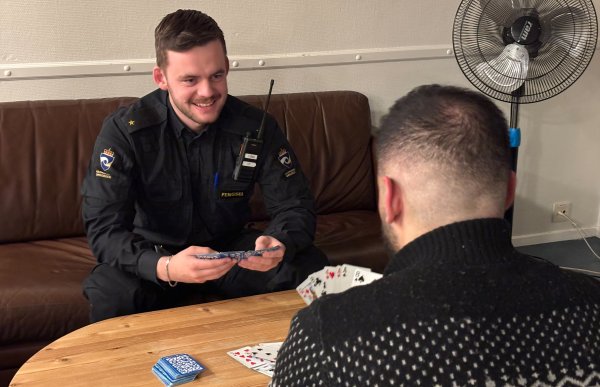 En mann i svart uniform og en mann i svart og hvit ullgenser sitter ved et bord og spiller kort