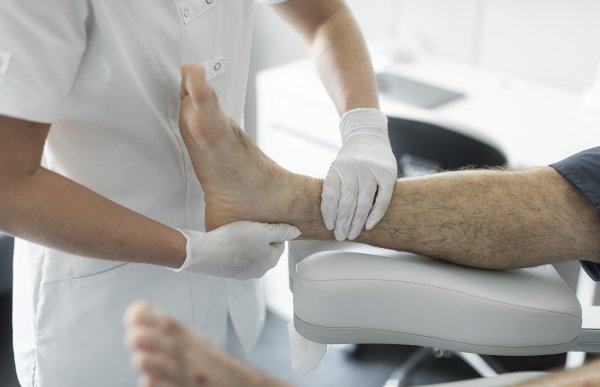 En person i hvit skjorte og plasthansker holder en fot som ligger på ei hvit pute. 