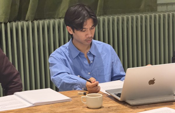 Mann med mørkt hår og blå skjorte sitter og reviderer manus. Han holder en penn, og foran ham ligger en PC, notatark og en kaffekopp.