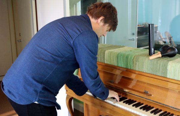 En mann i blå skjorte spiller på et gammelt piano.