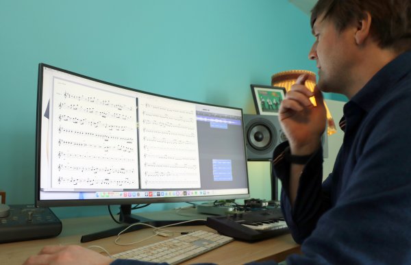En mann sitter foran en dobbel dataskjerm. På skjermene vises noter til en ny komposisjon.  