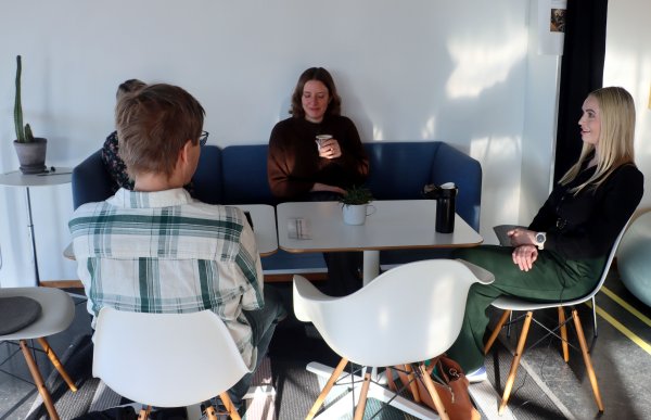 Fire mennesker sitter rundt et bord. Rommet er lyst og solen skinner inn på menneskene. 