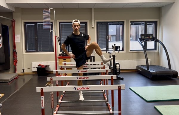 En mann med svart t-skjorte og shorts beveger seg over røde og hvite hinder i et stort treningsrom.