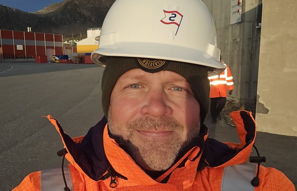 Mann i oransje uniform med hvit hjelm og refleks på skulderen. Han smiler til kamera.