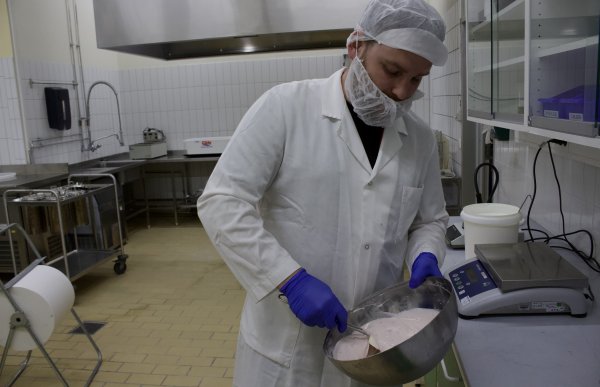Mann med hvit frakk, hvit beskyttelseshette på hodet og rundt munnen. Han rører rundt i en bolle med yoghurt. Han er i et laboratorium.