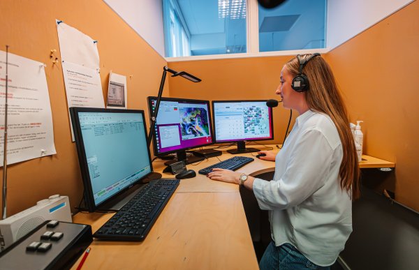 En kvinne sitter for seg selv i et radiostudio. Hun melder værmeldingen, og sitter med headset på hodet.