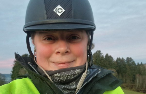 Dame med ridehjelm. Hun smiler og ser rett i kameraet.