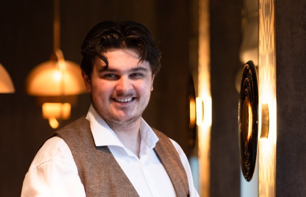 Mann i hvit skjorte og vest. Han smiler og ser rett i kameraet.