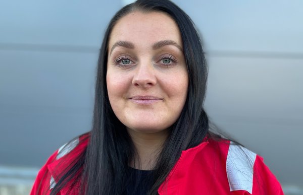 Portrettbilde av en dame med langt, svart hår. Hun har rød jakke på seg. I bakgrunnen er en grå, uklar bakgrunn.