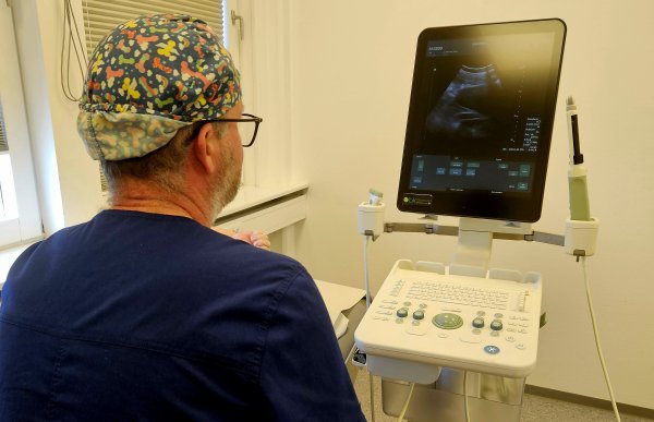 En mann i blå overdel ser på en ultralydmaskin. Han er på et legekontor.