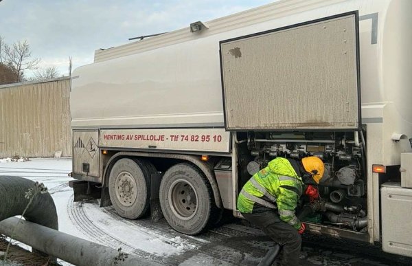 En mann i gul arbeidsjakke og hjelm bøyer seg ned og ser inn i motorrommet på en tankbil.