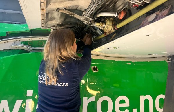 Dame med blå genser jobber med teknikken inne i et fly