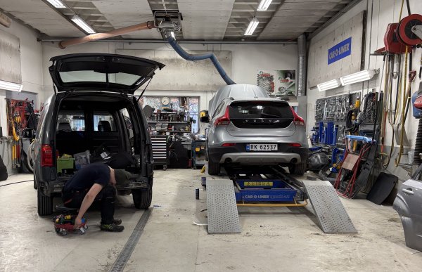 Et bilverksted der en person arbeider på en bil, mens en annen bil står på en løfteplattform for reparasjon.