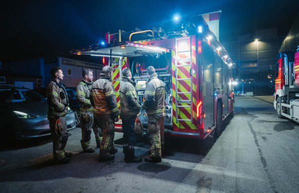 5 brannkonstabler står bak en brannbil. De tester nytt utstyr, og står sammen og diskuterer rundt en skjerm montert bak på bilen.