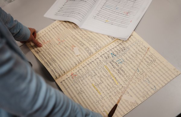 En person står lent over et bord, du ser bare armene. På bordet ligger noteblokker og en taktstav som dirigenter bruker.