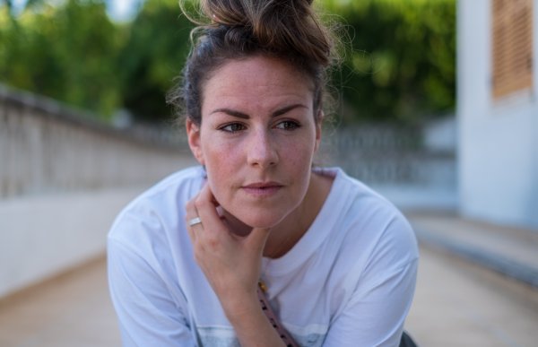 En kvinne i hvit t-sjorte og med oppsatt brunt hår utenfor et bygg.