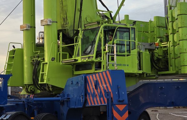 Kranfører Dorthe Sandvik på jobb. Dame i gule arbeidsklær sitter foran spakene i en stor, grønn kran.