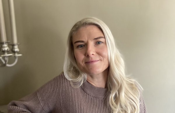 En dame med langt, blondt hår og lilla genser. Hun ser rett i kameraet og smiler.