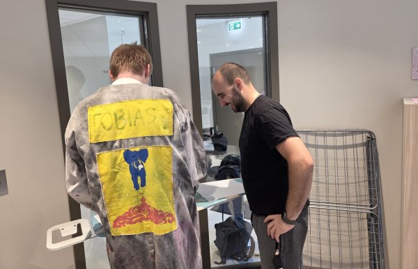 Skoleassistent Tommy Egeland hjelper en elev med stryking av klær To personer står over et strykebrett. Personen til venstre holder på å stryke et klesplagg mens personen til høyre følger med. De står i et hvitt rom med to dører som er åpne til andre rom.