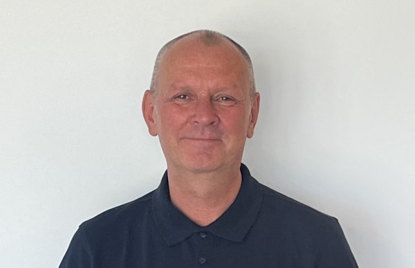 En mann i blå skjorte smiler mot kameraet.