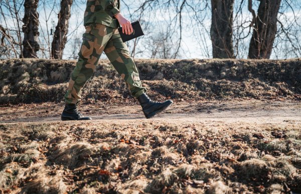 En person i uniform går langs en sti, fra venstre mot høyre. Den øverste halvdelen av kroppen er ikke synlig, men personen holder en notatbok i hånden.