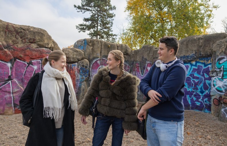 Tre ungdomer prater foran en fargerik graffitivegg utendørs.