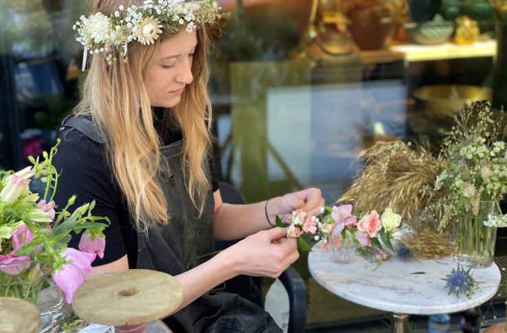 Blomsterdekoratør Ingrid Marie Aarre med blomsterkrans i håret lager en blomsterkrans med rosa blomster